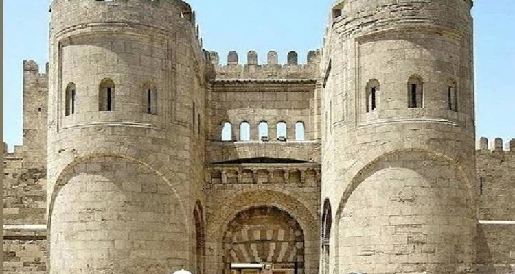 Medieval stone gate with two round towers and arched entrance under a clear sky.