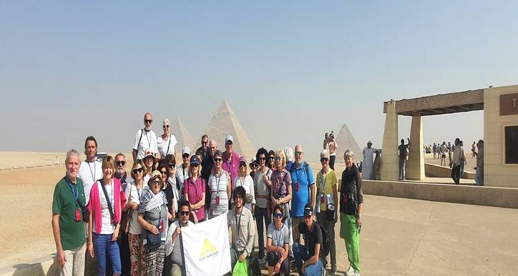 Large tour group gathered on a concrete platform with pyramids visible in the sand beyond.
