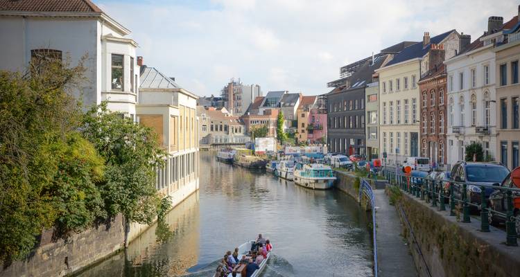 Un petit bateau de visite glisse le long d'un canal entre les bâtiments historiques de Gand par une belle journée.