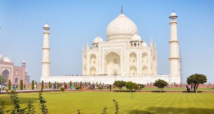 Classic frontal view of the Taj Mahal with manicured green lawns and blue morning sky.