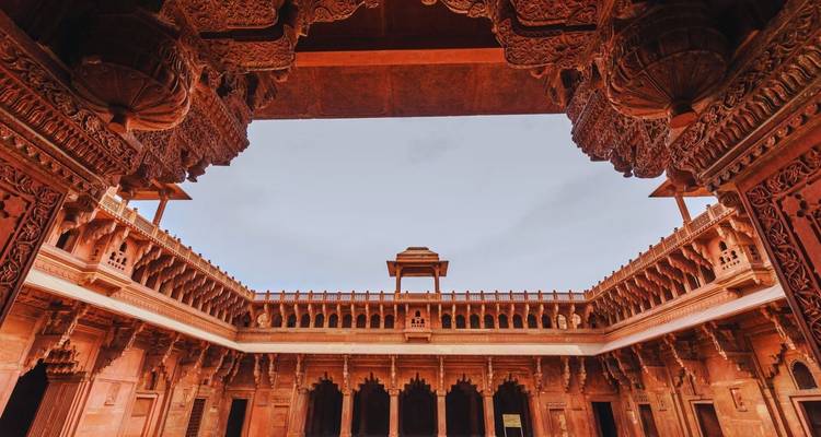 Upward view of an ornate red-sandstone courtyard framed by intricate carved eaves against a pale sky.