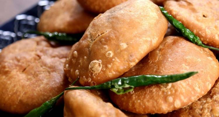 Close-up of golden fried pastries garnished with green chilies on a serving tray.