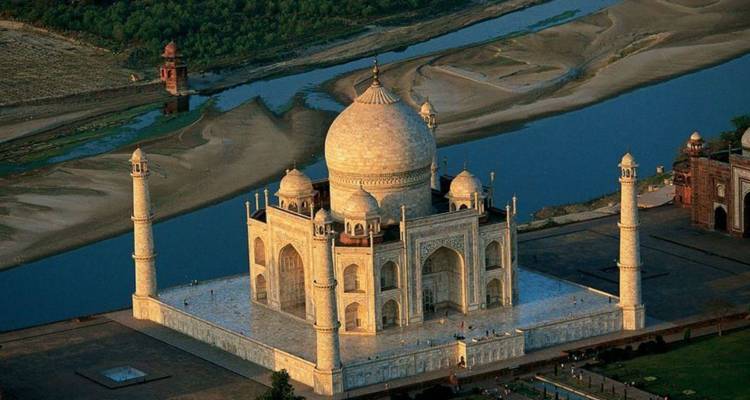 Aerial view of the Taj Mahal gleaming beside the winding Yamuna River at dawn.