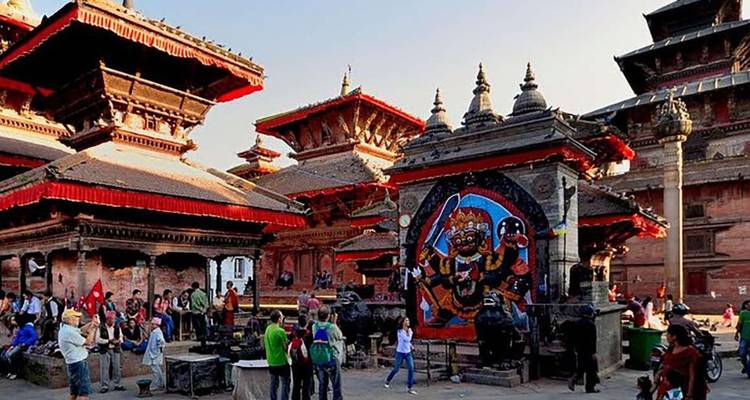 Busy square of tiered pagoda temples with vivid deity mural and crowds exploring heritage site.