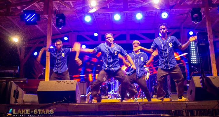 Nighttime dance troupe in blue uniforms performing energetically under bright stage lights.