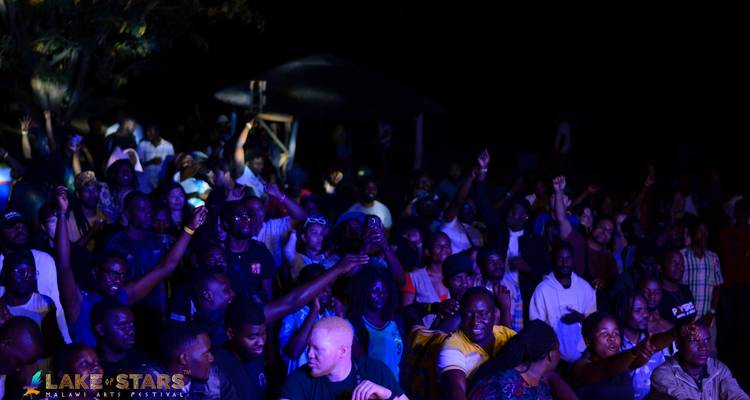 Nighttime festival crowd cheering in front of a dark stage area.