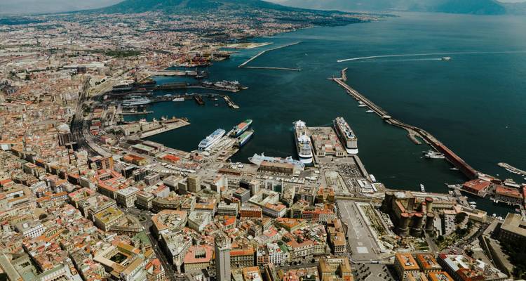 Panorama aérien élevé du port de Naples, navires de croisière et le Mont Vésuve se profilant au loin.