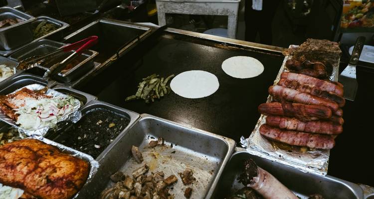 Marktgrillstation mit wärmenden Tortillas, Würstchen und verschiedenen Füllungen, die für Straßentacos bereit sind.