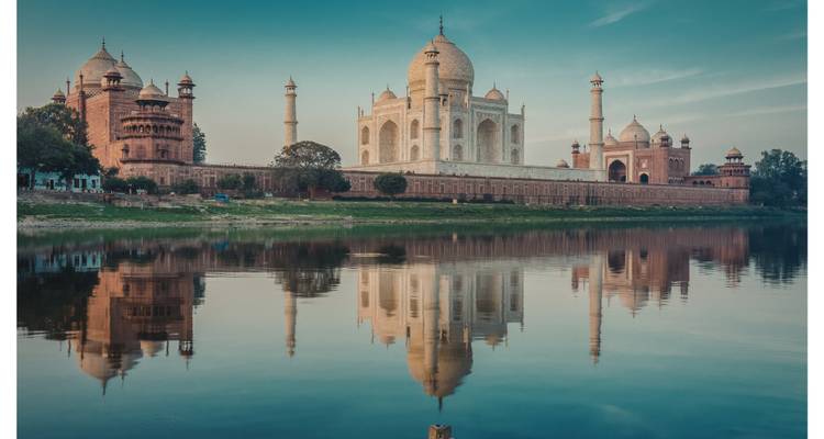 Iconic Taj Mahal perfectly reflected in the Yamuna River under a calm blue sky.
