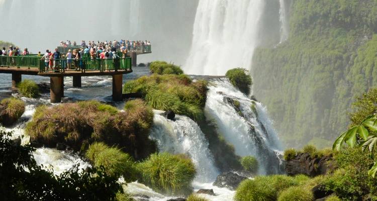 Crowds on a viewing platform overlook powerful Iguazu Falls cascading around lush islands.