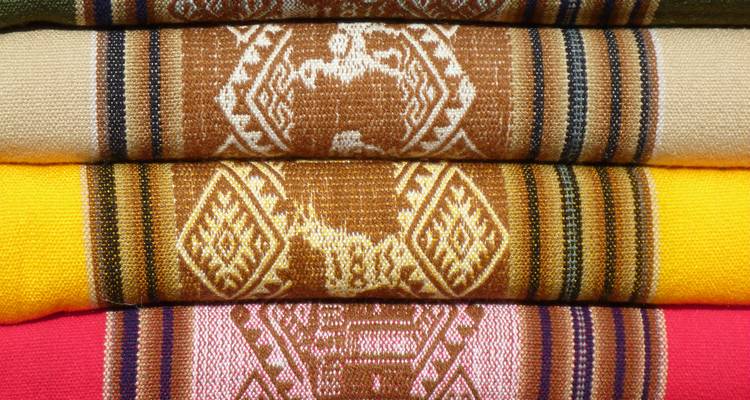 Stack of colorful woven Andean textiles with llama motifs.