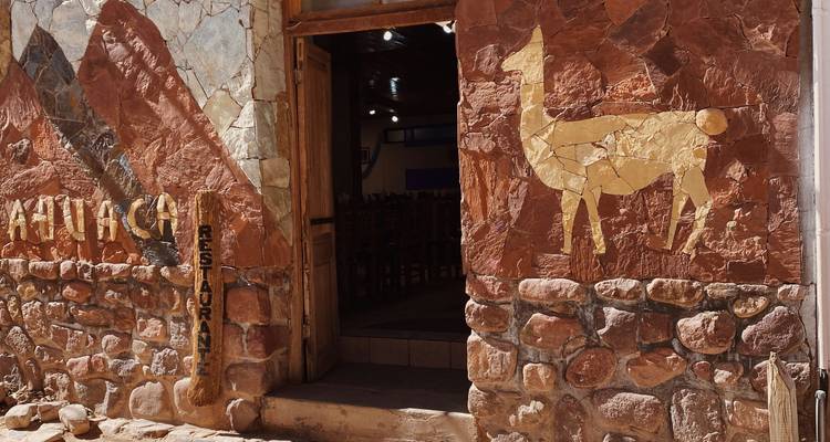 Rustic stone restaurant facade with llama mosaic in Andean village.
