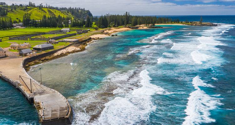 Aerial view of turquoise waters, rugged coastline and pier on lush Norfolk Island