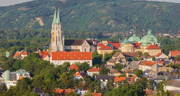 Picturesque old town with red-roofed houses and a slender cathedral spire against green hills.