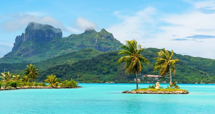 Turquoise lagoon with small palm-covered islet backed by the dramatic green peak of Mount Otemanu.