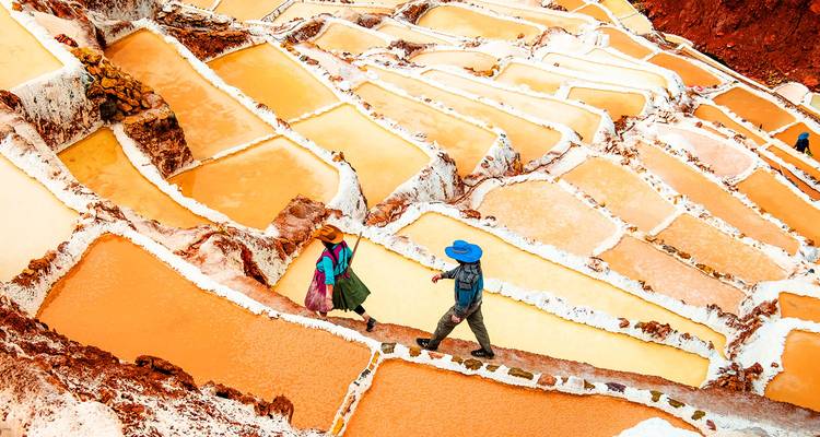 Vibrant terraced pools of orange salt at Maras with two traditionally dressed workers walking along narrow ridge.