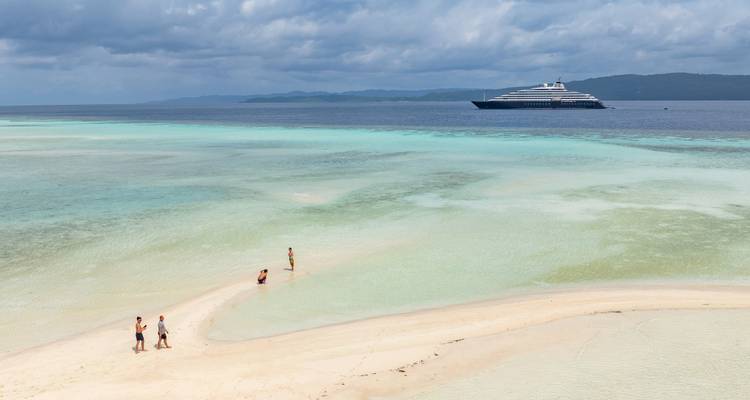 Tropical sandbar with small group wading, turquoise sea and luxury yacht offshore