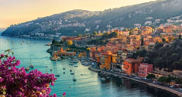 Les maisons pastel pittoresques s'étagent sur le flanc d'une baie de la Côte d'Azur parsemée de voiliers et encadrées par de brillantes fleurs de bougainvillée.