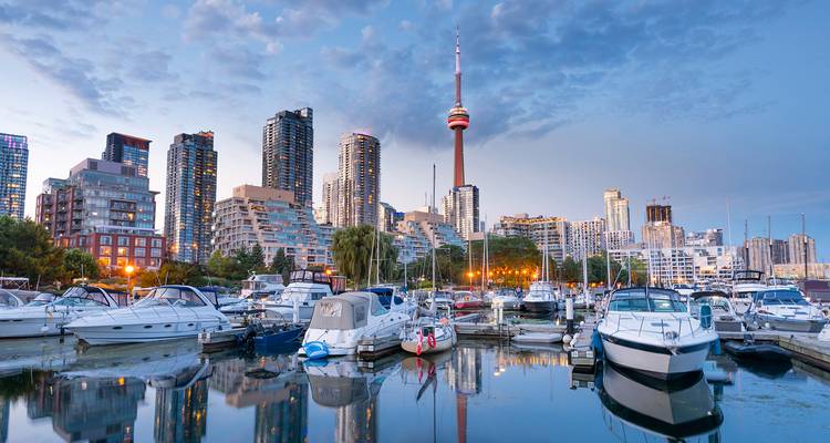 Marina with docked boats reflecting Toronto’s skyline and the CN Tower during soft evening light.