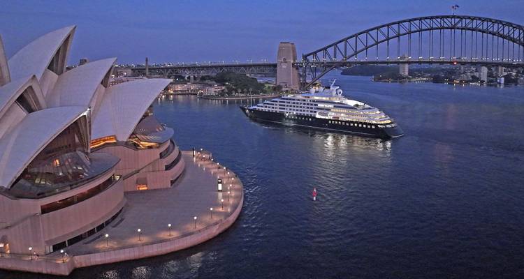 Sydney Opera House and Harbour Bridge at dusk with luxury expedition yacht cruising through the bay.