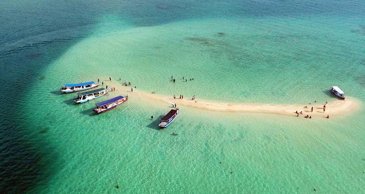 Crystal-clear turquoise lagoon with narrow sandbar where small boats are anchored and visitors stroll.