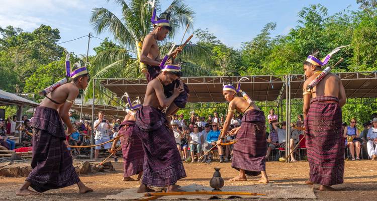 Traditional Indonesian warriors in colorful woven sarongs performing a spirited bamboo-stick dance before an audience.