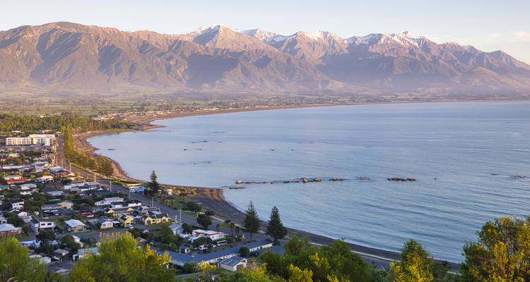 Panoramic view of Kaikoura township with sweeping bay and snow-dusted Seaward Kaikoura Range at sunrise.