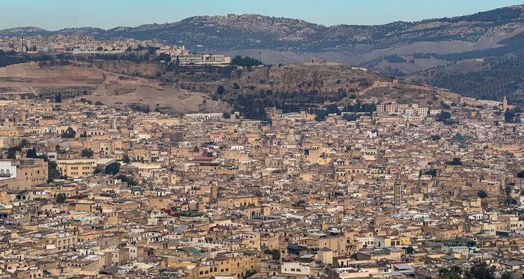 Panoramablick über die dichten Dächer der Medina von Fès vor dem Hintergrund zerklüfteter Hügel.