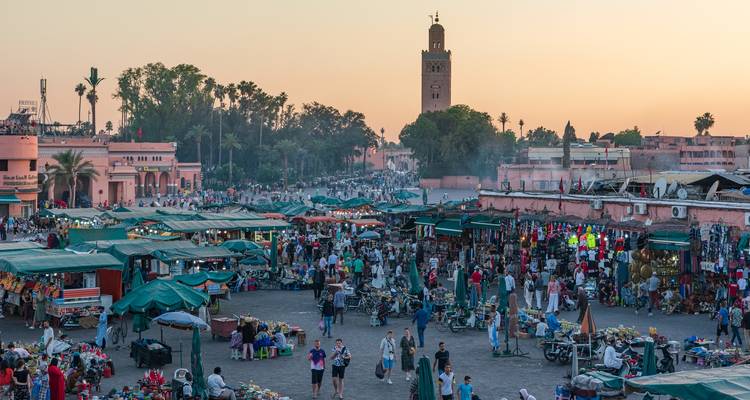 Geschäftiger Jemaa el-Fnaa Markt in der Abenddämmerung mit der Koutoubia-Moschee im Hintergrund.