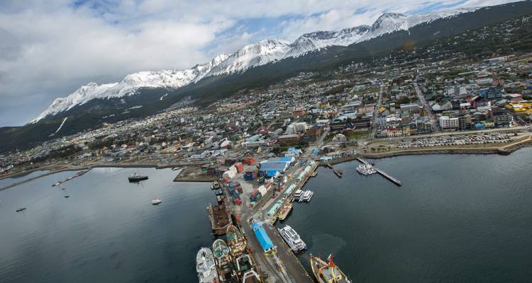 Luchtfoto van de haven van Ushuaia met sneeuwgebekte pieken en de uitgestrekte stad langs de kustlijn.