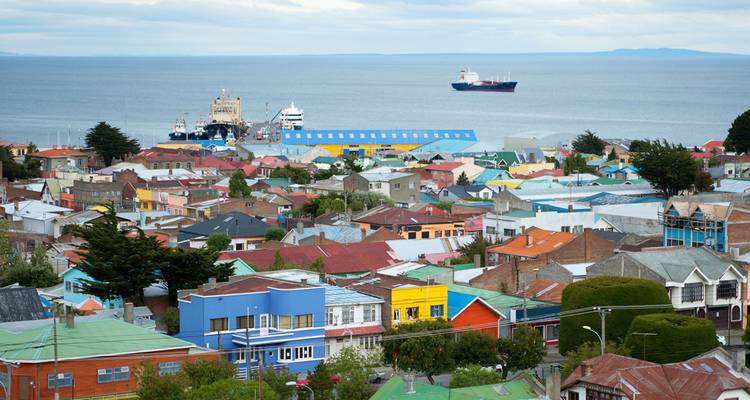 Coloridas casas de techo bajo en un pueblo costero con barcos anclados en el mar bajo cielos nublados.