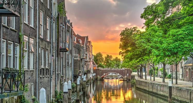 Serene sunset glow over tree-lined canal and historic Dutch houses in Dordrecht.