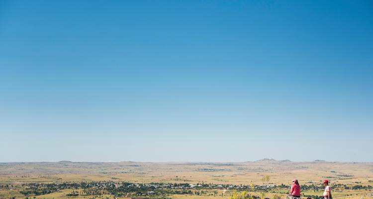 Un enorme cielo azul domina una meseta semiárida donde dos pequeñas figuras admiran el paisaje distante.