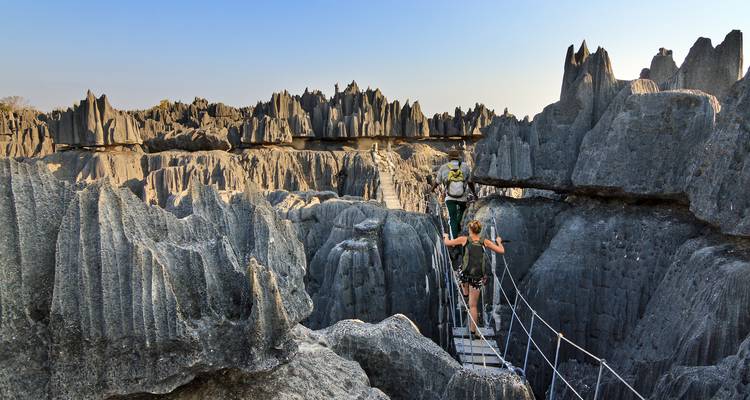 Los aventureros cruzan un puente colgante estrecho rodeados de los dramáticos y dentados picos de caliza del Tsingy.