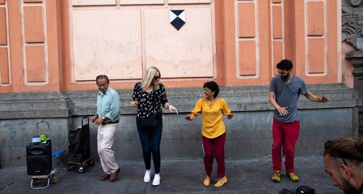 Toeristen voegen zich bij de lokale bevolking voor een levendige groepsdans op een stenen straat in Lima's historische centrum.