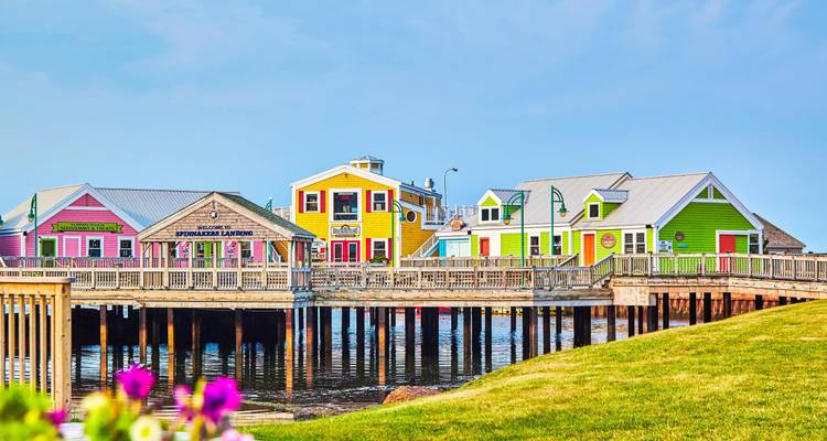 Façade maritime joyeuse de boutiques et restaurants en bois aux couleurs vives sur une jetée au-dessus d'une eau calme.