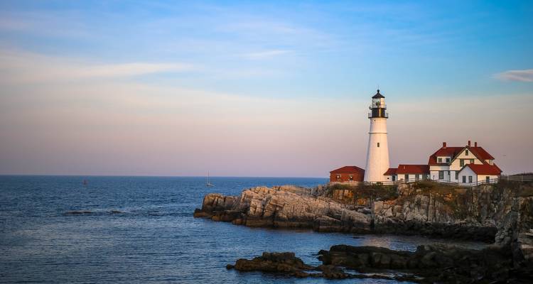 Portland Head Lighthouse on a rocky Maine coast at dusk with soft pastel sky.