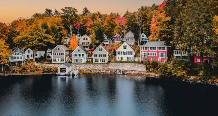 Charming row of colorful lakeside houses backed by vibrant autumn trees reflecting in calm water.