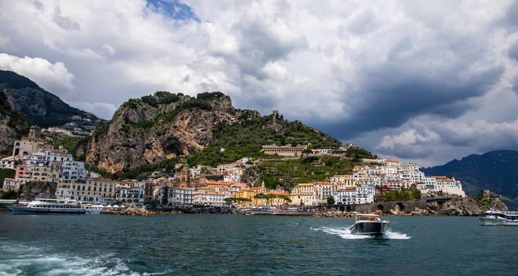 Amalfi town nestled against steep cliffs viewed from sea with dramatic sky