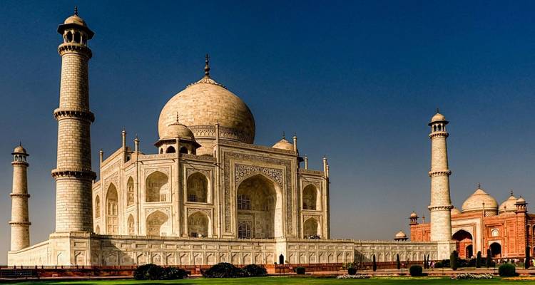 Iconic view of the Taj Mahal with its minarets and marble dome glowing under a clear blue sky.