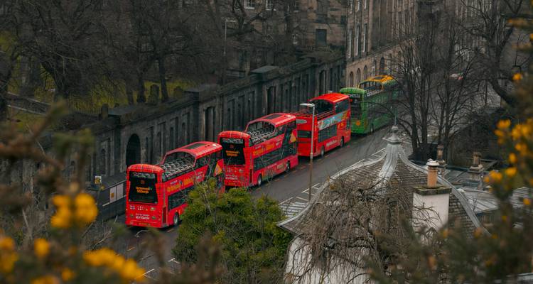 Rangée d'autobus touristiques rouge vif et vert à arrêts multiples garés à côté de murs en pierre historiques à Édimbourg.