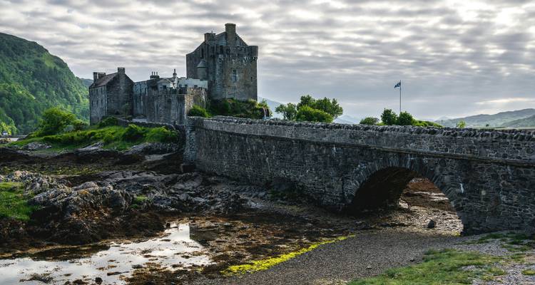 Ciel morose au-dessus du château d'Eilean Donan et du pont de pierre se reflétant dans les eaux peu profondes des marées.