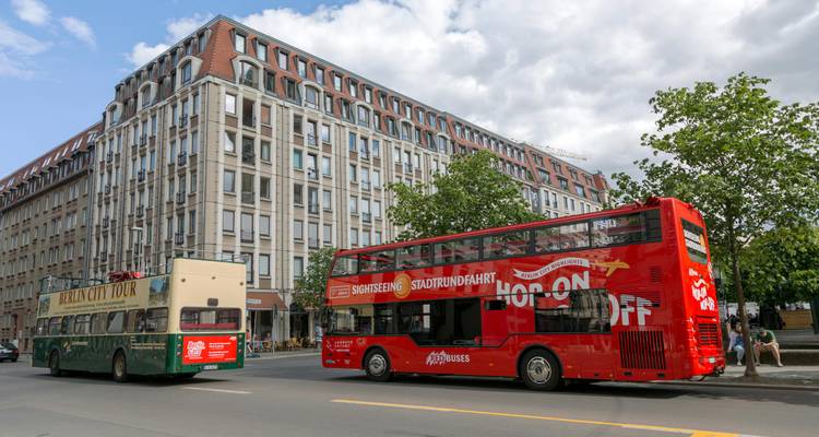 Scène de rue urbaine avec des autobus à impériale rouges et crème de tourisme devant un bâtiment moderne.