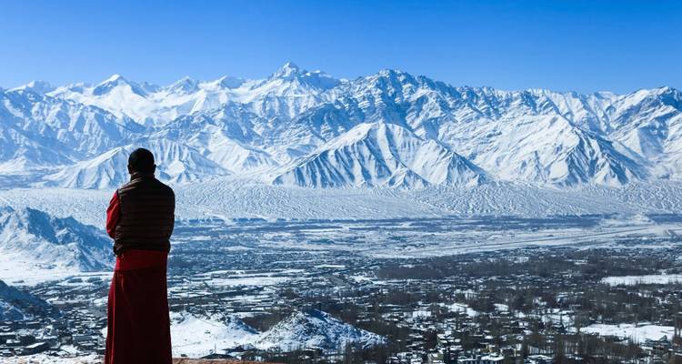 Robe-clad monk gazing over snow-clad Himalayan peaks and the valley town of Leh.