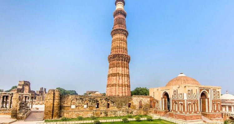Tall red-sandstone Qutub Minar towering above historic complex on a hazy day.