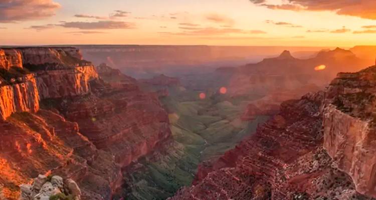Grand Canyon vista glowing in warm sunrise light with deep red cliffs.