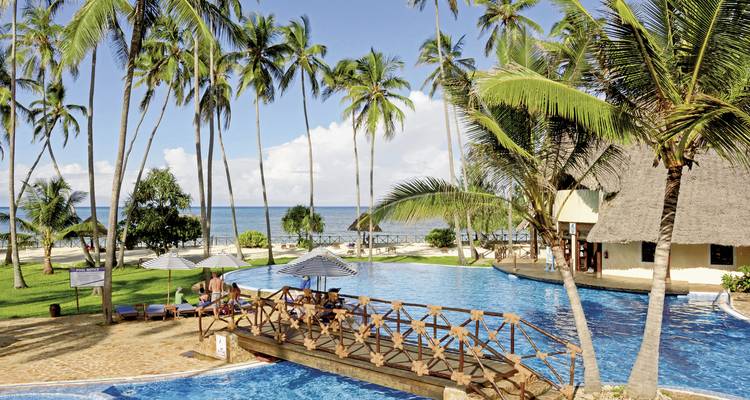 Hotelpool umgeben von Palmen mit Meerblick, Gäste entspannen auf Liegestühlen