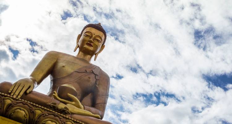 Large golden Buddha statue against a partly cloudy sky in Bhutan.