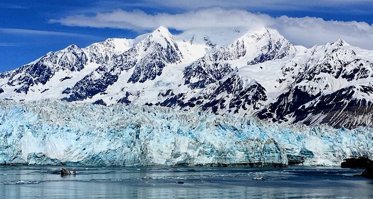 Towering snow-covered peaks and a vivid blue glacier meet calm water under a crisp sky in Alaska.