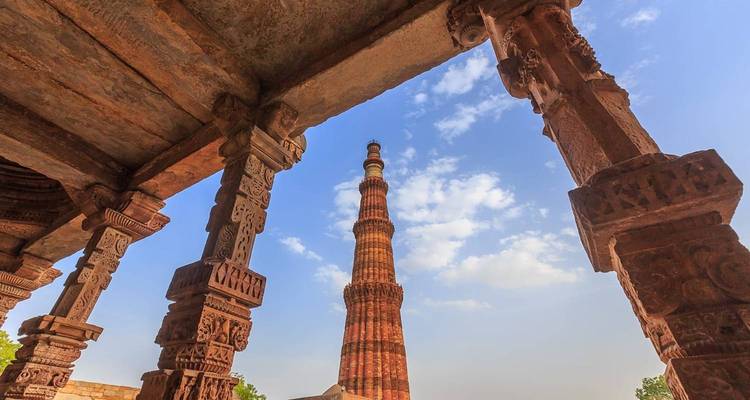 Vista de la torre Qutub Minar enmarcada por pilares de piedra ornamentalmente tallados